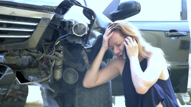 自動車事故の概念。女性ドライバーは、壊れた車のバンパーに座って交通事故の後に電話をかけます — ストック動画