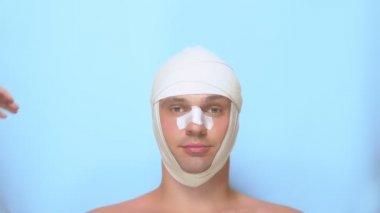 Plastik cerrahi kavramı, bir adamın yüzünü tutan eller. plastik cerrahi den sonra bir adam facelift, burun estetiği, burun da bandaj ile, baş. mavi arka planda.