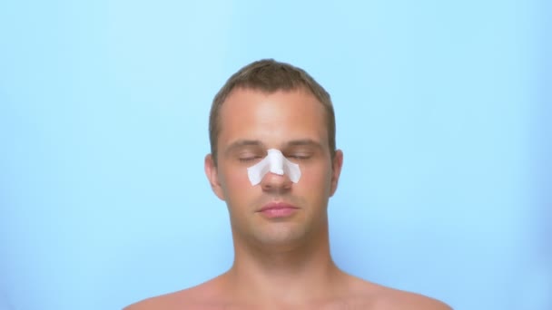 Begreppet plastikkirurgi, en man efter en plastikkirurgi i ansiktet, näsplastik, med ett bandage på näsan. på blå bakgrund. — Stockvideo