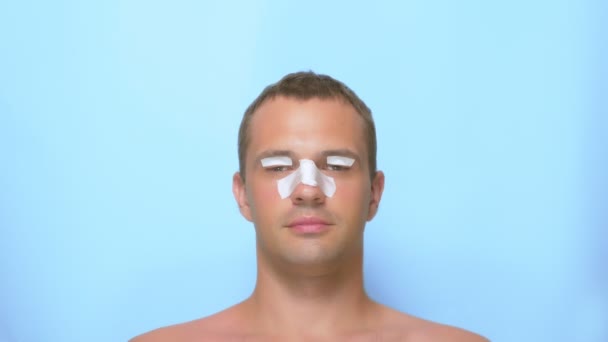 El concepto de cirugía plástica, un hombre después de una cirugía plástica en la cara, rinoplastia y blefaroplastia, con un vendaje en la nariz y los párpados. sobre fondo azul . — Vídeos de Stock