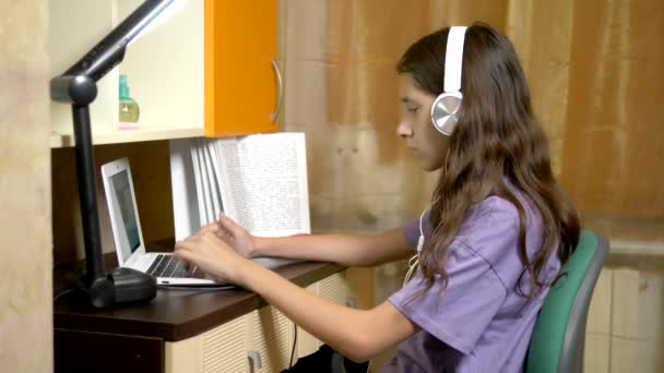 Estudante aprendendo on-line com um laptop branco sentado em uma mesa em seu quarto adolescente. à noite — Vídeo de Stock