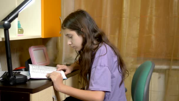 Studente ragazza legge un libro mentre seduto a tavola nella sua stanza adolescenti. in orario serale — Video Stock