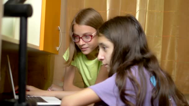 Две девушки подруги, подростки студенты сидят вместе за тренировочным столом и используют ноутбук в вечернее время. они веселы и счастливы — стоковое видео