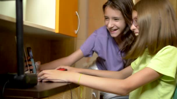 Dos chicas amigas, estudiantes adolescentes se sientan juntas en la mesa de entrenamiento y usan una computadora portátil por la noche. son alegres y felices — Vídeo de stock