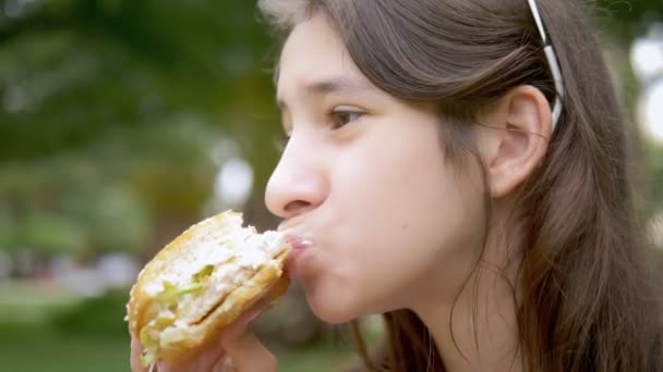 Le concept d'un pique-nique d'été. Gros plan. Adolescente mange un hamburger de poulet assis dans un parc. gros plan . — Video