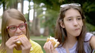 Öğrenciler piknik kavramı. iki kız kız parkta çim üzerinde oturan hamburger ve patates yiyor