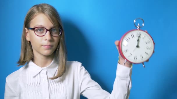 O conceito de tempo de aprendizagem, de volta à escola. uma estudante com óculos detém um grande relógio e está surpreso que chegou a hora de aprender. no fundo azul — Vídeo de Stock