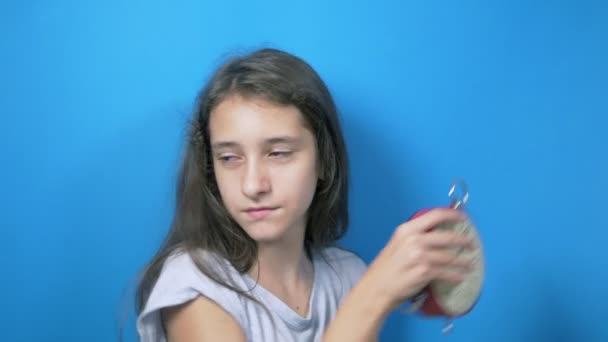 The concept of learning time, back to school. Schoolgirl holds a big clock, pointing at them and smiling, that it is time to learn. on blue background — Stock Video