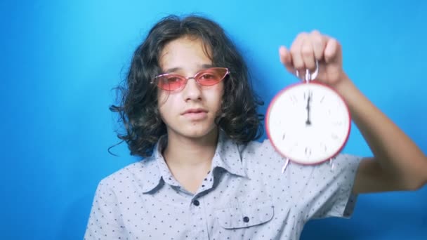 Grappige tiener in roze bril houdt een klok in haar handen, kijkt naar de tijd en sluit haar gezicht met haar hand. — Stockvideo