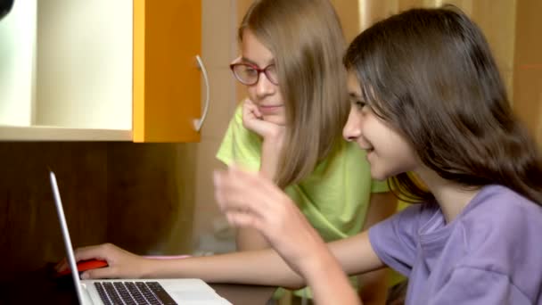 Dos chicas amigas, estudiantes adolescentes se sientan juntas en la mesa de entrenamiento y usan una computadora portátil por la noche. son alegres y felices — Vídeos de Stock