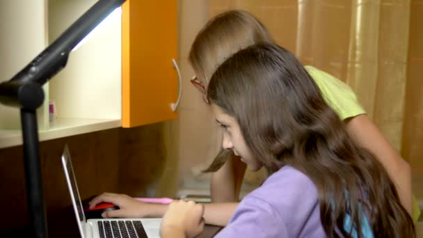 Дві дівчини-подружки, студенти-підлітки сидять за тренувальним столом і користуються ноутбуком ввечері. вони веселі і щасливі — стокове відео