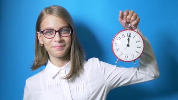 Concept van studietijd, terug naar school. Een smart girl schoolmeisje met bril houdt een grote klok en toont een super teken. — Stockvideo