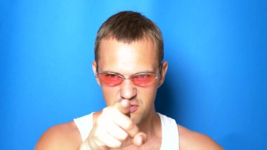mavi bir arka plan üzerinde pembe gözlük yakışıklı eğlenceli adam, dans ve komik yüzler yapma. Portre. kopyalama alanı