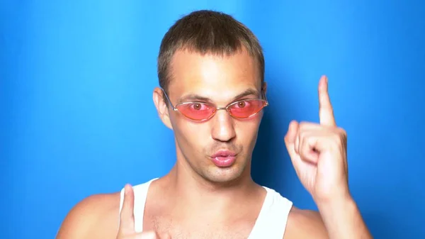 Przystojny figlarny facet w różowe okulary na niebieskim tle, taniec i podejmowania śmieszne twarze. Portret. miejsce kopiowania — Zdjęcie stockowe