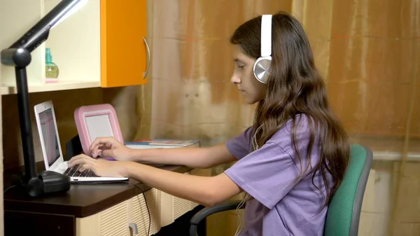 Student Girl lärande på rad med en vit laptop sitter vid ett bord i hennes tonårs rum. i kvällstid — Stockfoto