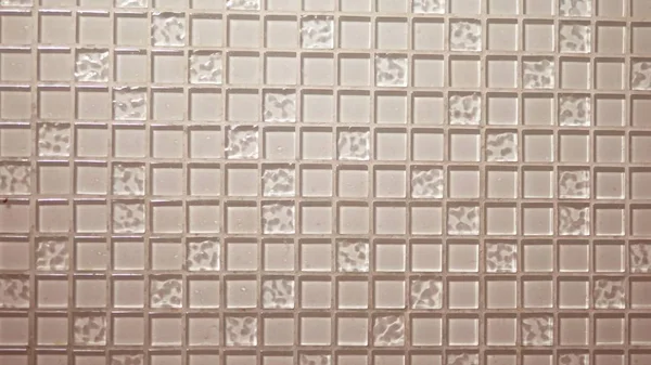 Texture background beige mosaic, small square transparent tiles on the wall. Glass panel for the kitchen