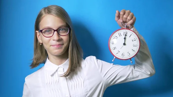 Konzept des Zeitstudiums, zurück zur Schule. ein smartes Schulmädchen mit Brille hält eine große Uhr und zeigt ein Superzeichen. — Stockfoto