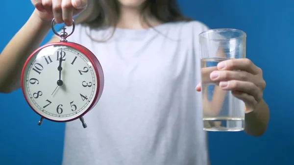 Conceito de dieta. A menina está segurando um despertador e um copo de água. tempo para beber água — Fotografia de Stock