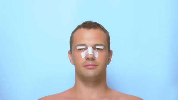 Het concept van plastische chirurgie, een man na een plastische chirurgie op het gezicht, rhinoplastiek en blepharoplastie, met een verband op de neus en oogleden. op blauwe achtergrond. — Stockfoto