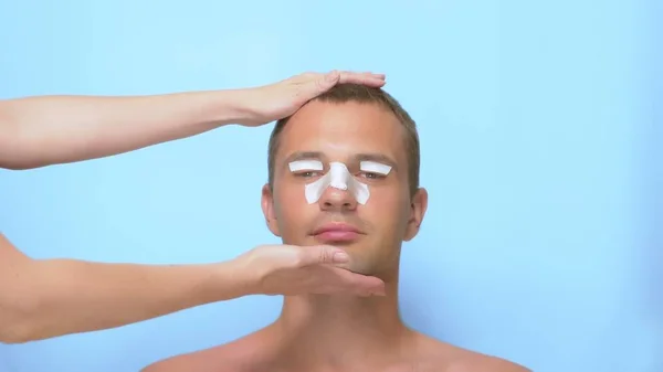 Plastic surgery concept, hands holding a mans face. a man after a plastic surgery on the face, rhinoplasty and blepharoplasty, with a bandage on the nose and eyelids. on blue background. — Stock Photo, Image