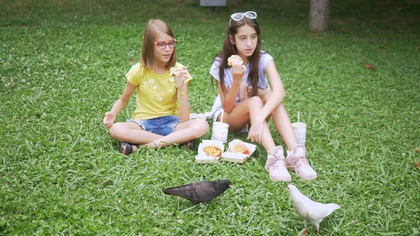 Chicas lindas se sientan en la hierba en el parque y alimentar a los pájaros papas fritas —  Fotos de Stock