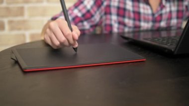 Yakın. Kalem kullanan ekose gömlekli genç bir çocuğun eli. grafik tabletüzerinde çalışır