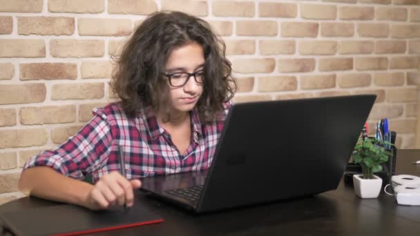 Zamknij. chłopiec nastolatek z kręcone włosy brunetka, w koszulę Plaid działa na tablecie graficznym za pomocą rysik — Wideo stockowe