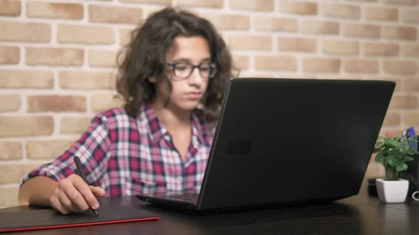 Közel. tinédzser fiú göndör barna haja, a kockás inget dolgozik egy grafikus tabletta segítségével ceruzával — Stock Fotó
