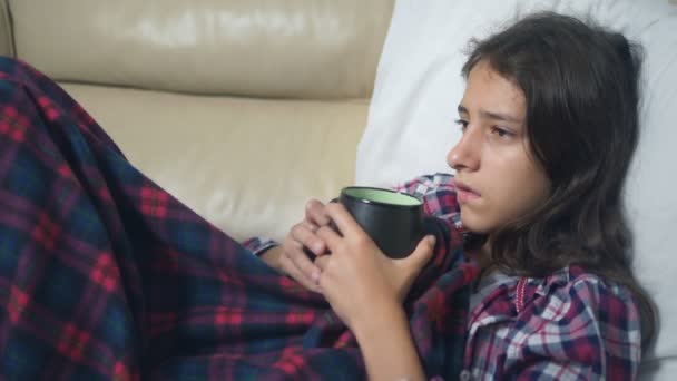 Zieke tiener meisje onder de covers drinkt een warm drankje op de Bank — Stockvideo