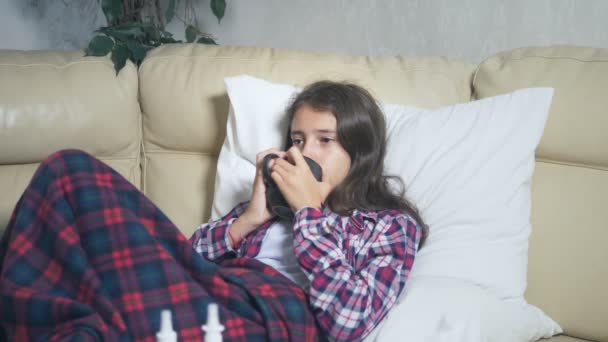 Хвора дівчина-підліток під обкладинками п'є гарячий напій на дивані — стокове відео