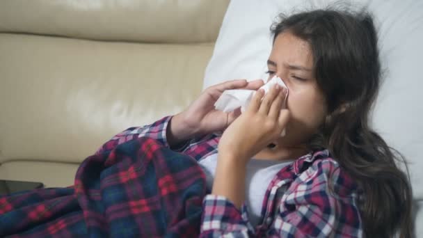 Adolescente avec un froid souffle son nez couché sur le canapé sous les couvertures . — Video