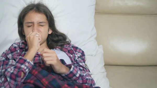 Teenager girl with a cold blows her nose lying on the sofa under the covers. — Stock Photo, Image