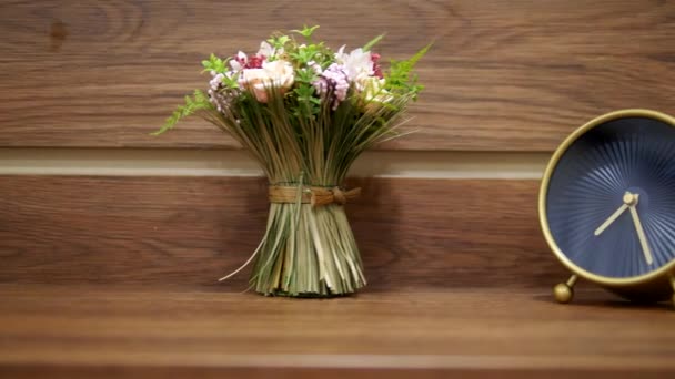 Relógio de alarme elegante e um pequeno buquê de flores artificiais na mesa de cabeceira — Vídeo de Stock