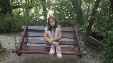 parkta bir salıncak üzerinde sallanan üzgün genç kız