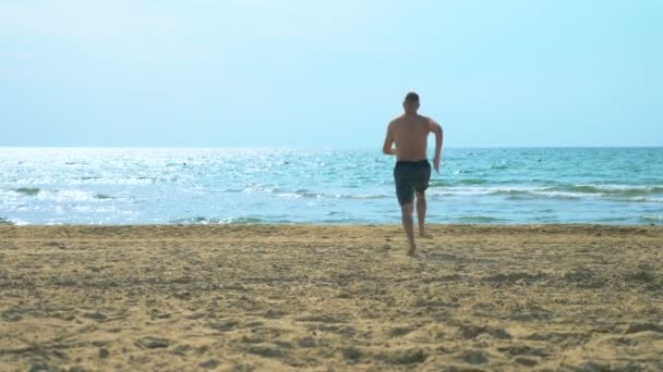 Junger Mann läuft an einem Sandstrand auf See — Stockvideo