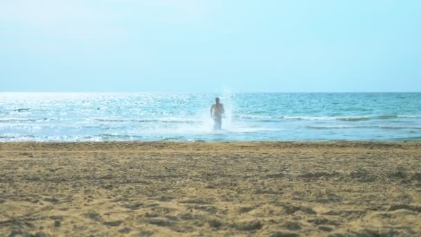 Молодой человек бегает по песчаному пляжу в море — стоковое видео