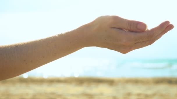 Sand strømmer gjennom fingre mot bakgrunnen av hav og himmel – stockvideo