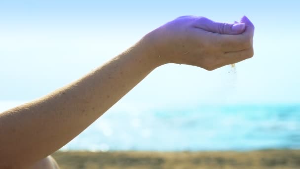 Zand stroomt door de vingers tegen de achtergrond van de zee en de lucht — Stockvideo