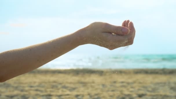 Песок течет сквозь пальцы на фоне моря и неба — стоковое видео