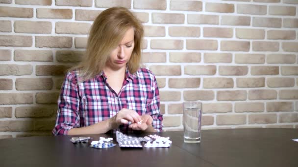 Άρρωστη θλιμμένη γυναίκα ταξινομεί τα χάπια ενώ κάθεται στο τραπέζι. υγεία και έλλειψη βιταμινών. — Αρχείο Βίντεο