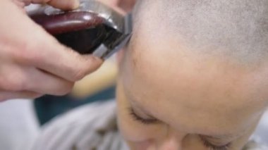 Kuaför elektrikli jiletle bir kadının kafasındaki saçı tıraş ediyor. Yakından kapatın. profesyonel bir saç makinesi ile saç kesme