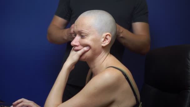 Man shaves a bald woman with an electric razor on a blue background. chemotherapy effects concept. — Stock Video