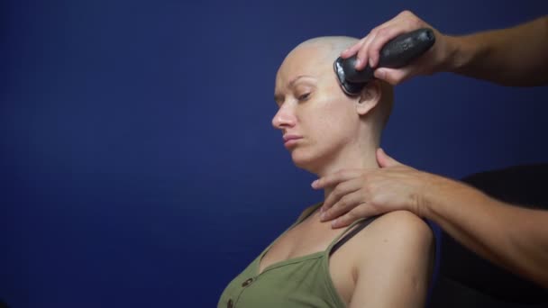 Man shaves a bald woman with an electric razor on a blue background. chemotherapy effects concept. — Stock Video