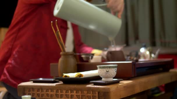 Китайський чашку чаю в різкість, на розмитому тлі процесу традиційного китайського пиття чаю. Майстер наливає чай в чашки — стокове відео
