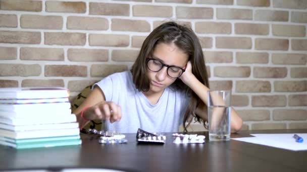 Conceito de saúde, avitominose durante cargas de treinamento. adolescente menina classificando pílulas sentado em uma mesa com livros didáticos e notas — Vídeo de Stock