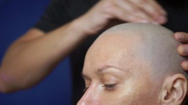 Adam mavi bir arka plan üzerinde elektrikli bir jilet ile kel bir kadın tıraş. kemoterapi etkileri kavramı.