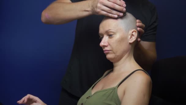 Muž oholí plešatou ženskou s elektrickým břitvou na modrém pozadí. koncepce působení chemoterapie. — Stock video