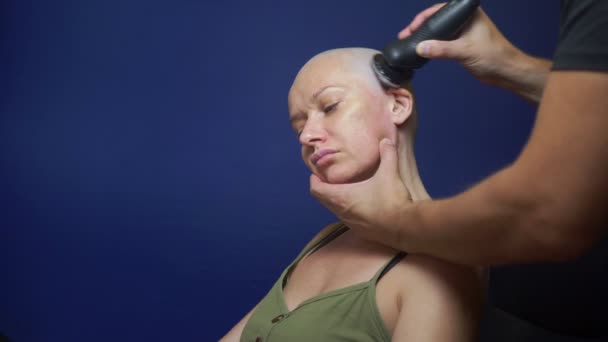 Ember borotválja kopasz nőt egy elektromos borotvát a kék háttérben. kemoterápiás hatások koncepció. — Stock videók