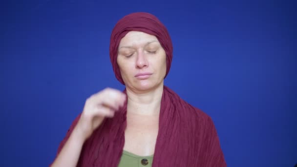 Calvo donna esausta su uno sfondo blu guarda la fotocamera. Si sente a disagio a causa della caduta dei capelli. concetto di oncologia e gli effetti della chemioterapia — Video Stock