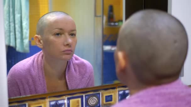 Стильная лысая женщина вытирает лицо салфеткой, глядя в зеркало в ванной комнате . — стоковое видео